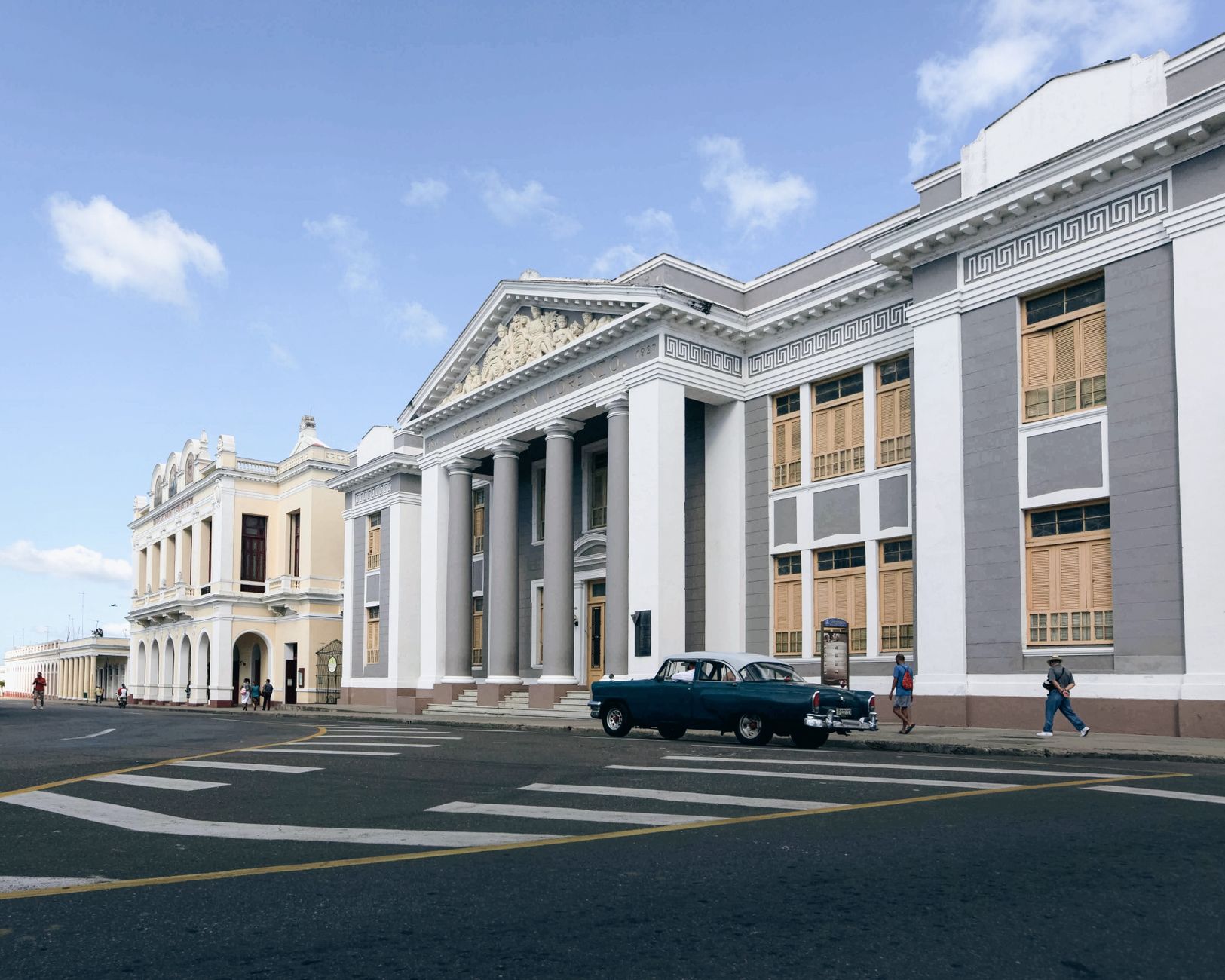 Elegant neoclassical building in Cuba with vintage car and pedestrians on street.