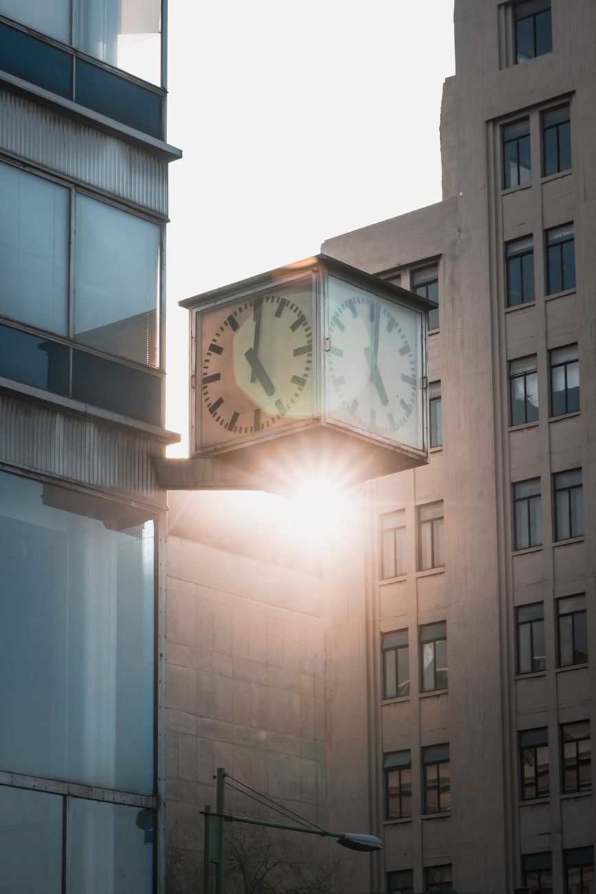 Urban street clock on building facade with sunlight, showcasing modern architecture and time theme.