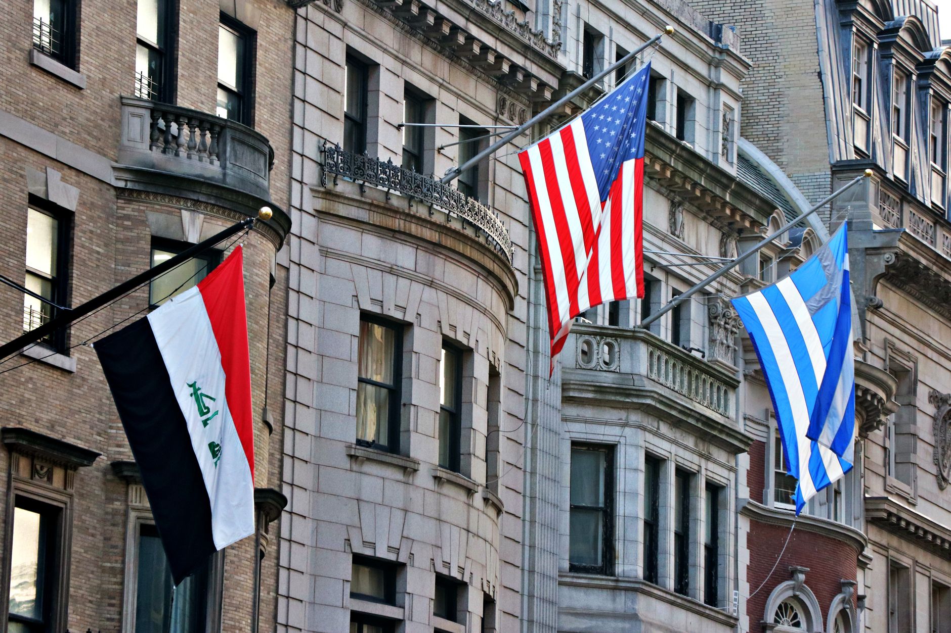 Three national flags displayed on historical city buildings in daytime.