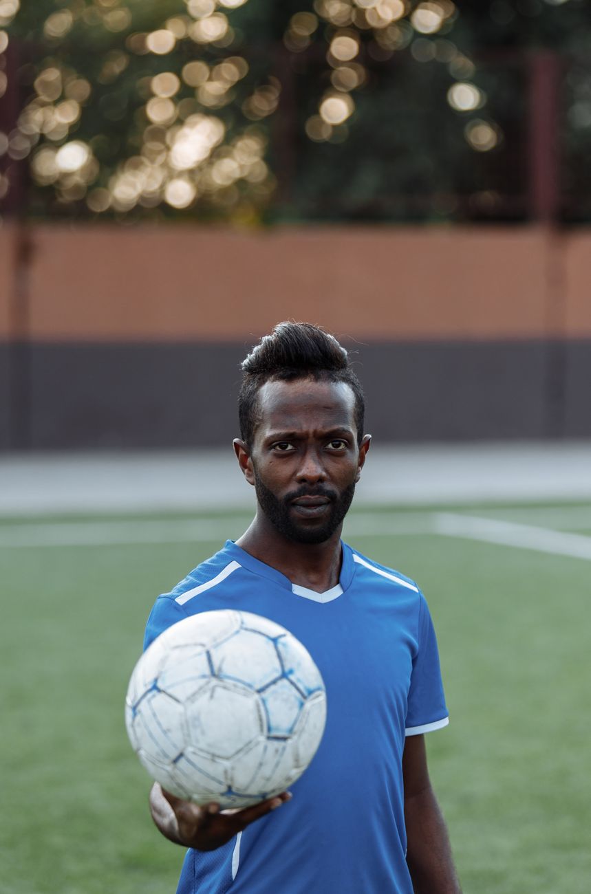 Portrait of a bearded African American man holding a soccer ball on an outdoor field.