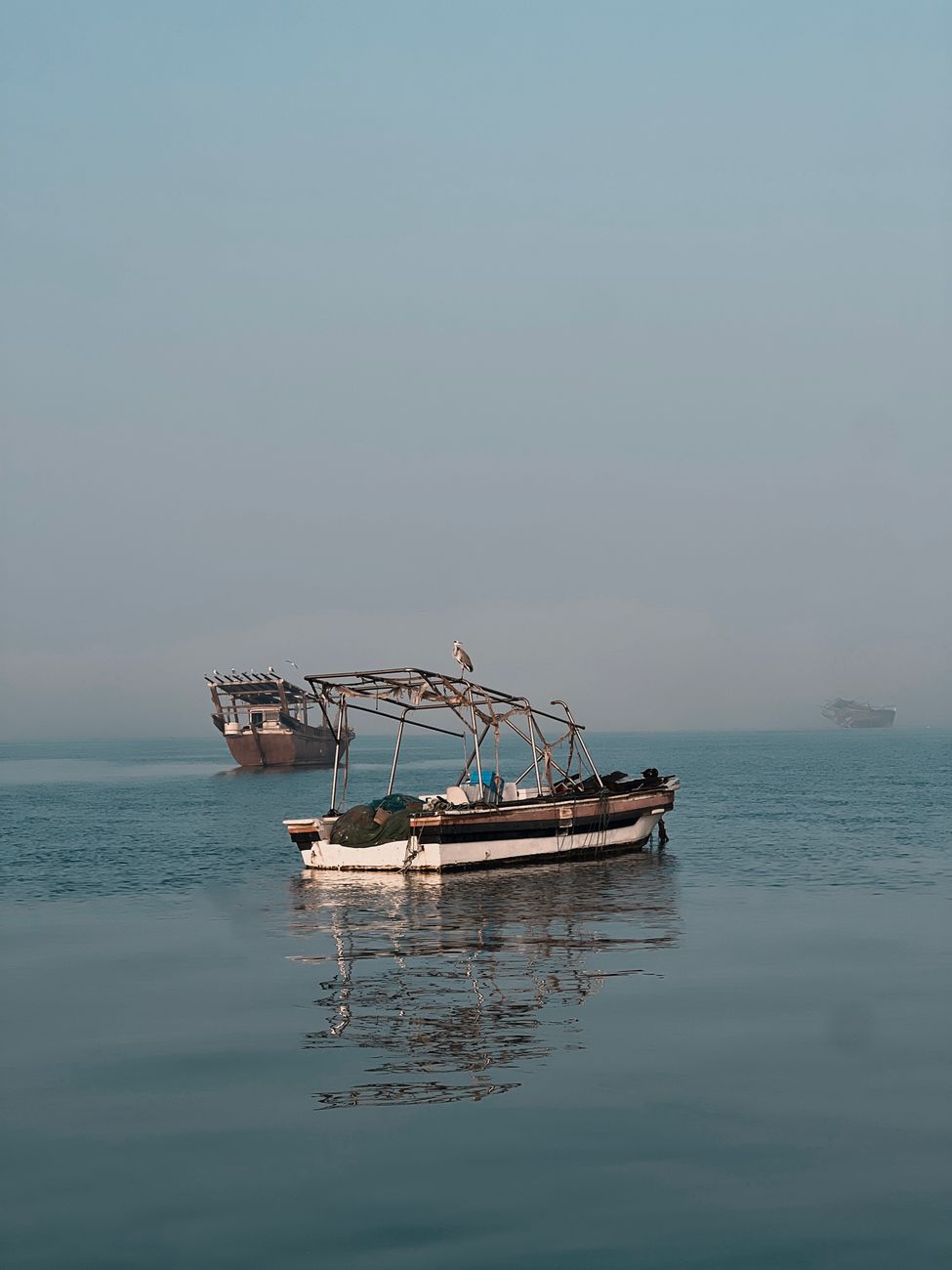 Traditional boats floating on calm sea near Manama, Bahrain, in a serene, misty morning.
