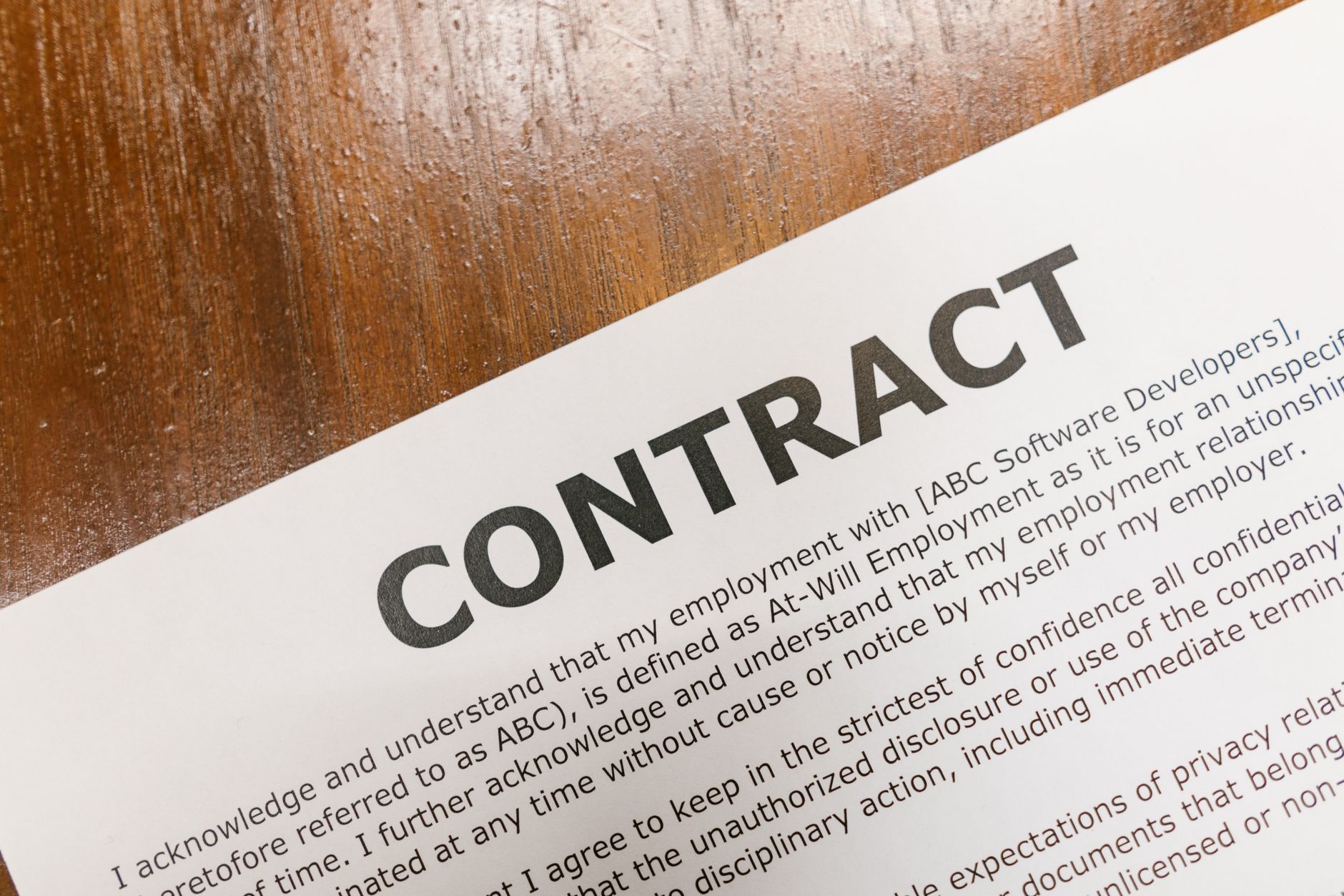 A detailed close up of a printed contract document on a wooden table surface.