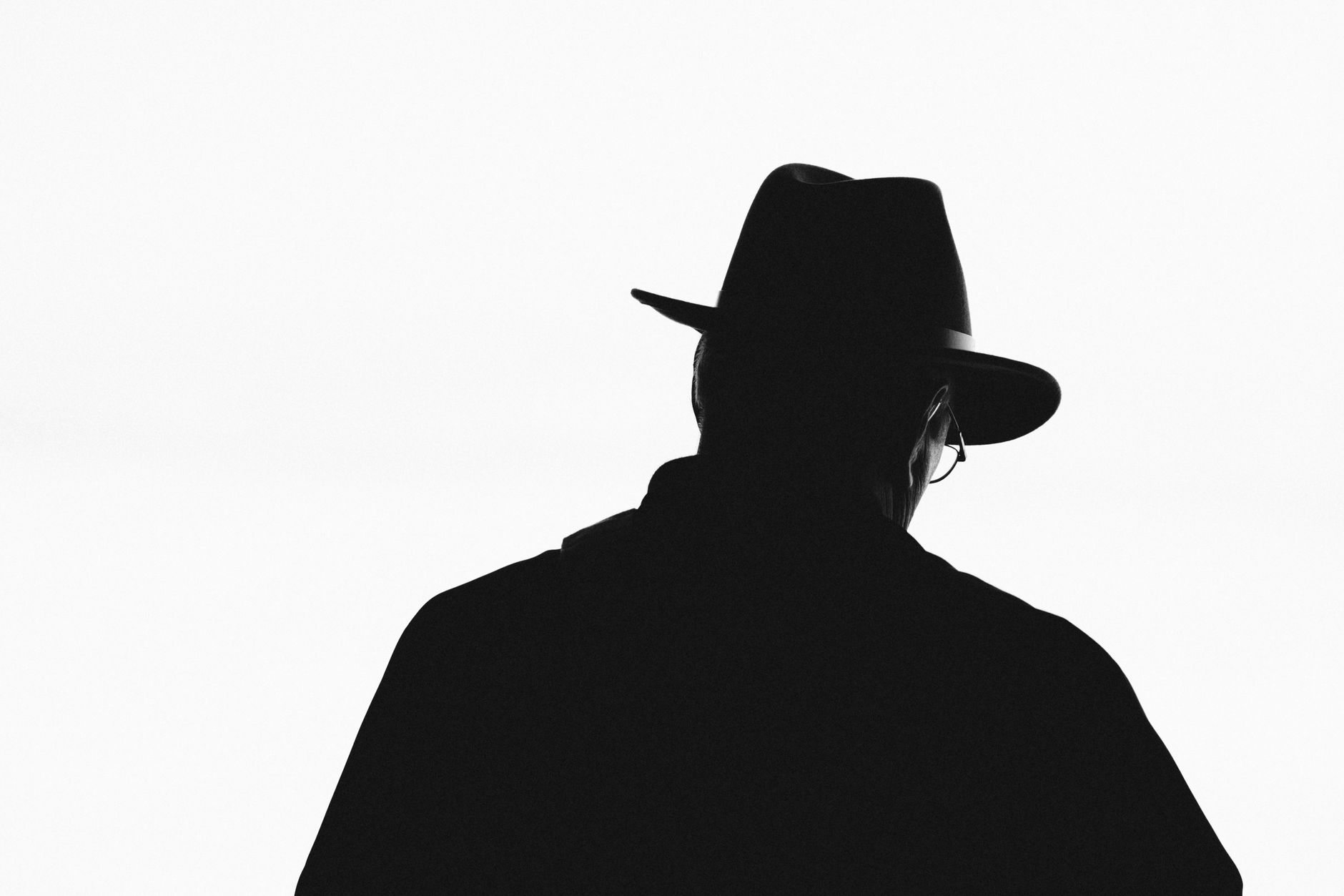 Striking back view silhouette of a man in a hat against a white background.