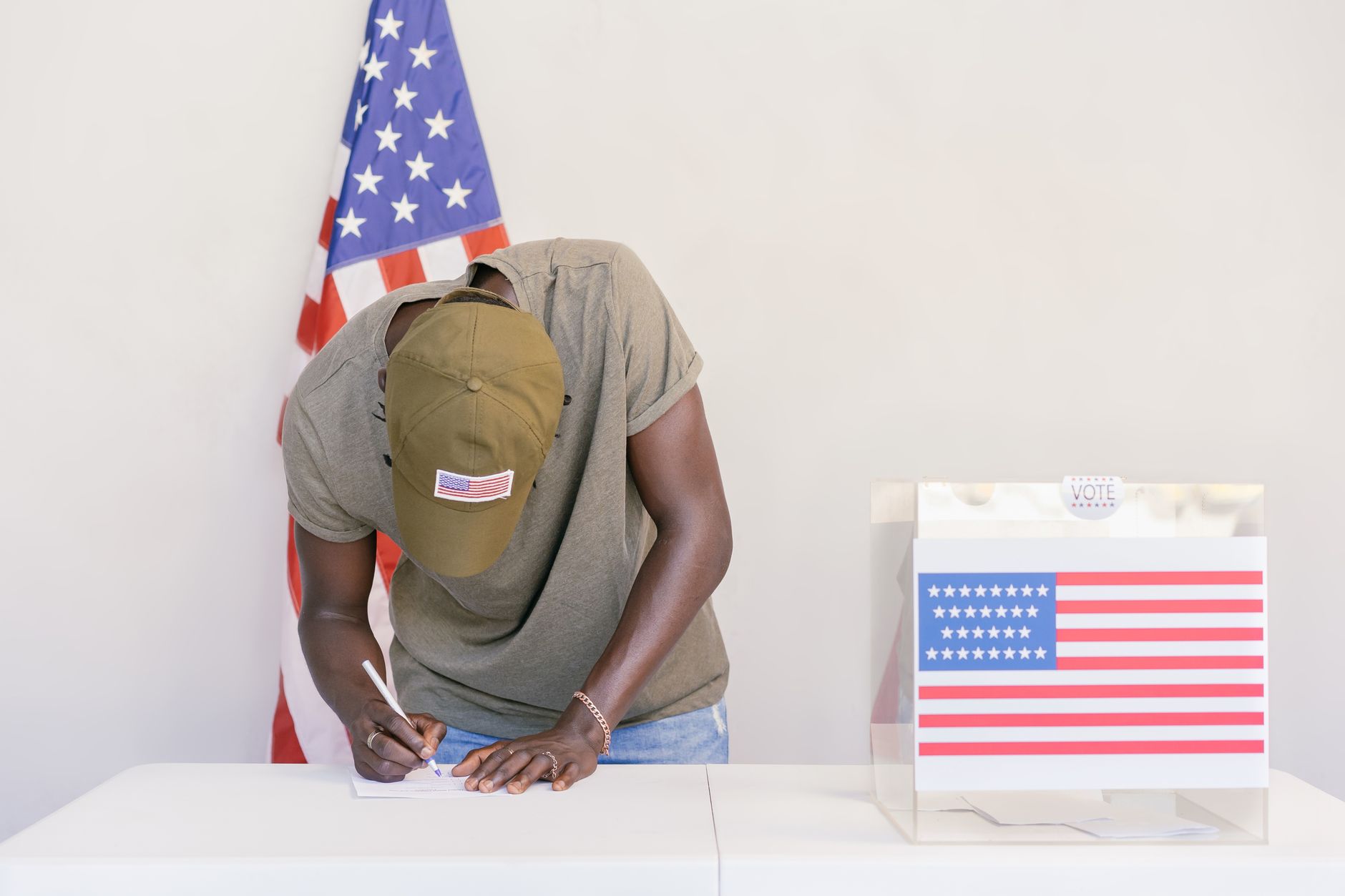 Man casting vote at polling station with American flag in background.