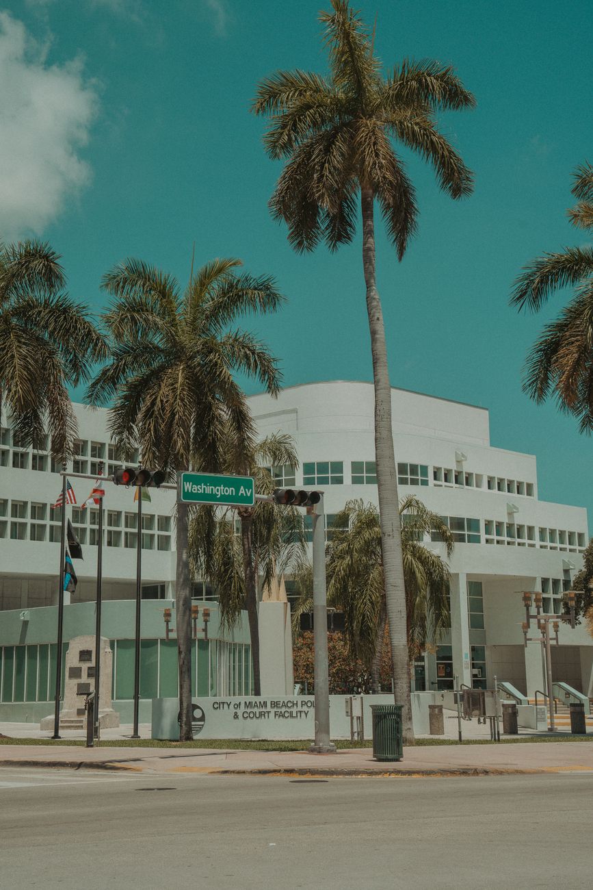 View of Miami Beach Police station on Washington Avenue with palm trees under clear blue sky.