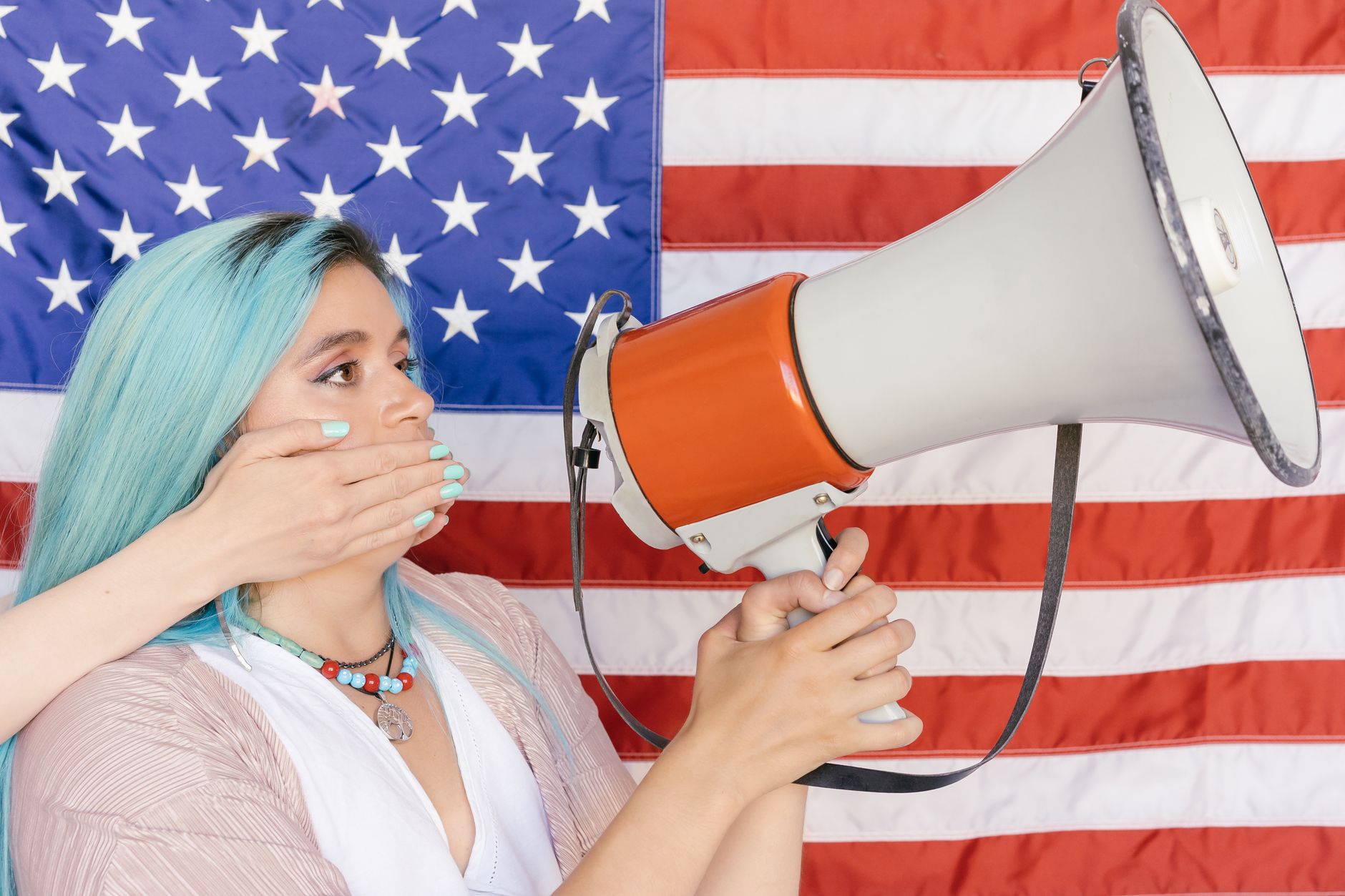 Woman holding megaphone with hand over mouth in front of American flag.