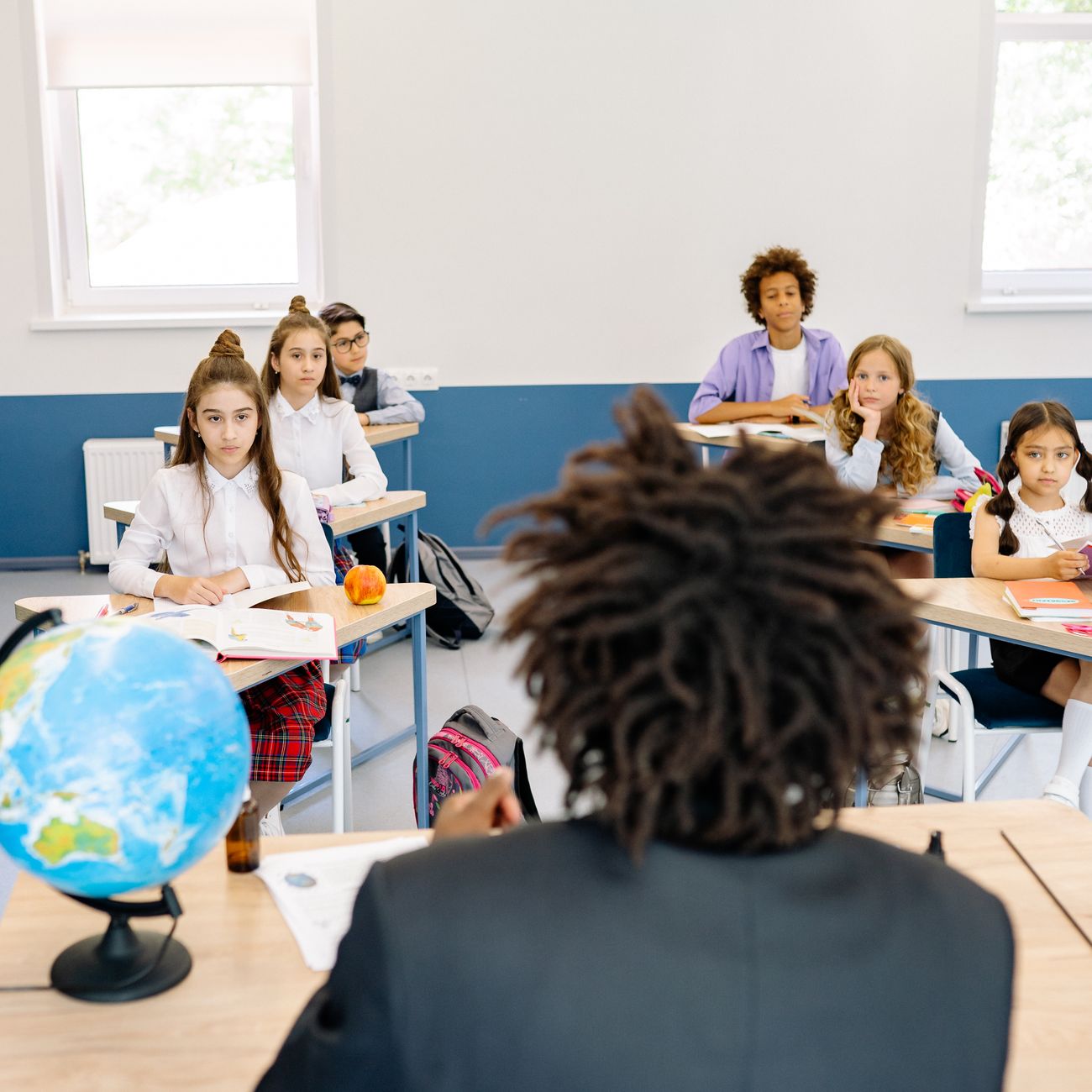 Diverse group of students attentively listening to teacher in bright classroom.