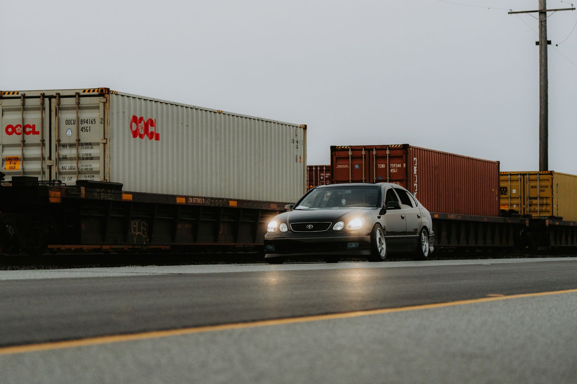 A car passing by a railway crossing with freight containers loaded on a stationary train.