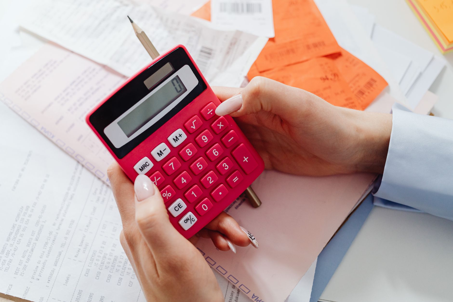 Close up of hands holding a red calculator, managing finances with documents and receipts.