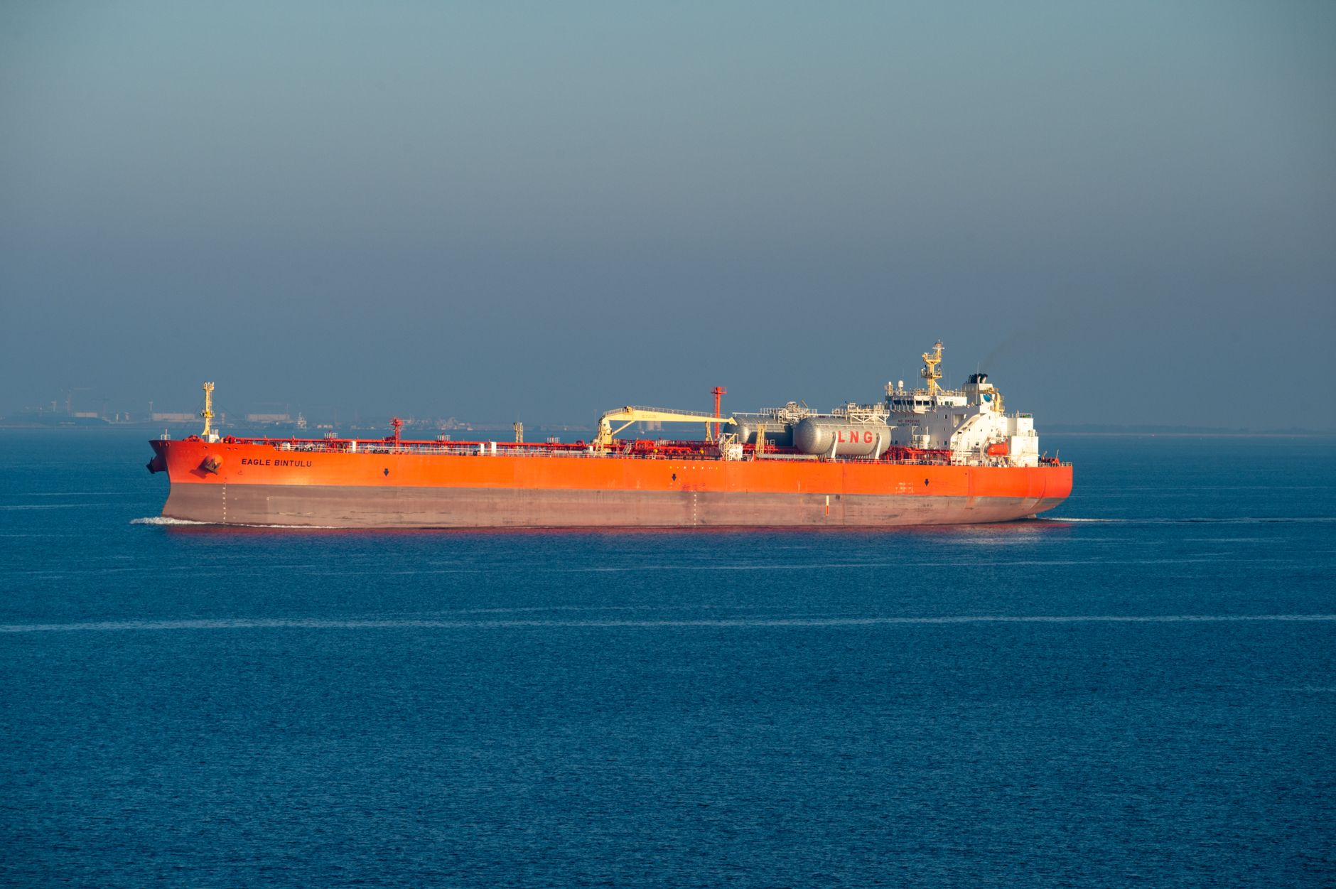 Bright orange LNG carrier ship cruising through calm sea waters on a clear day.