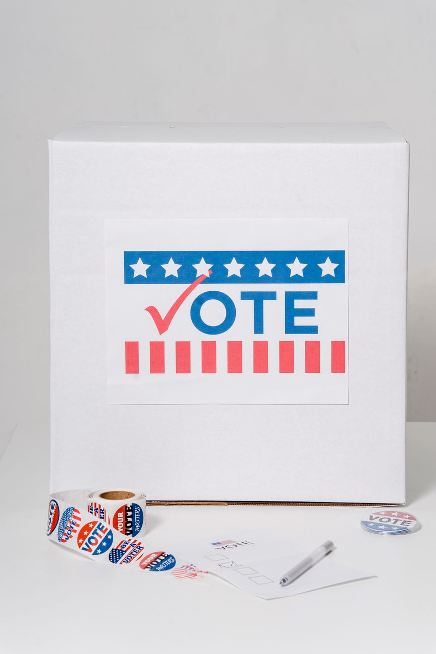 Ballot box with &amp;#39;Vote&amp;#39; sign and voting stickers on a white background.