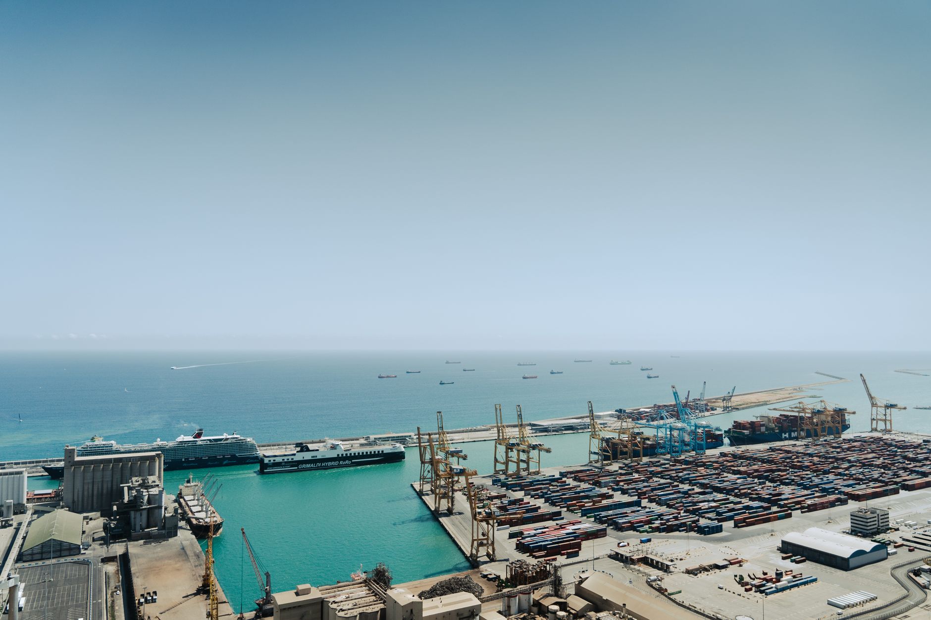 Stunning aerial shot of the bustling Port of Barcelona featuring cargo containers and cruise ships.