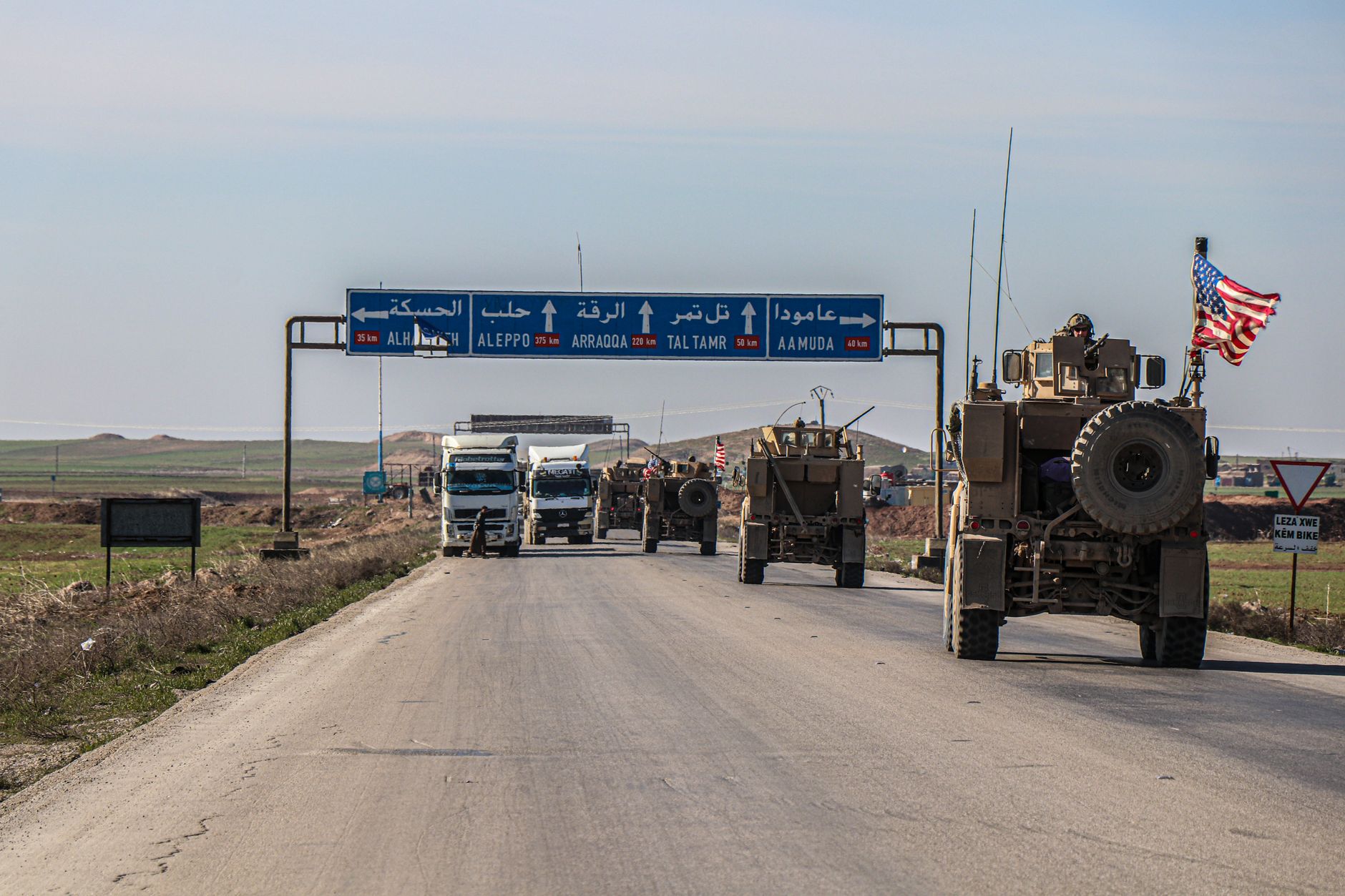 US military convoy travels on a highway in Al Hasakah, Syria, under blue skies.