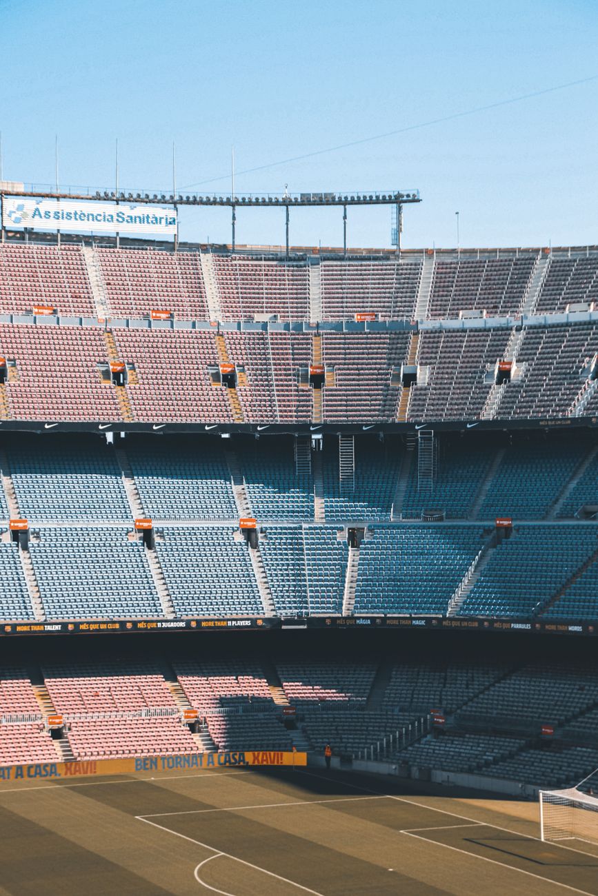 An empty soccer stadium with tiered seating under a clear blue sky, capturing shadows and sunlight.