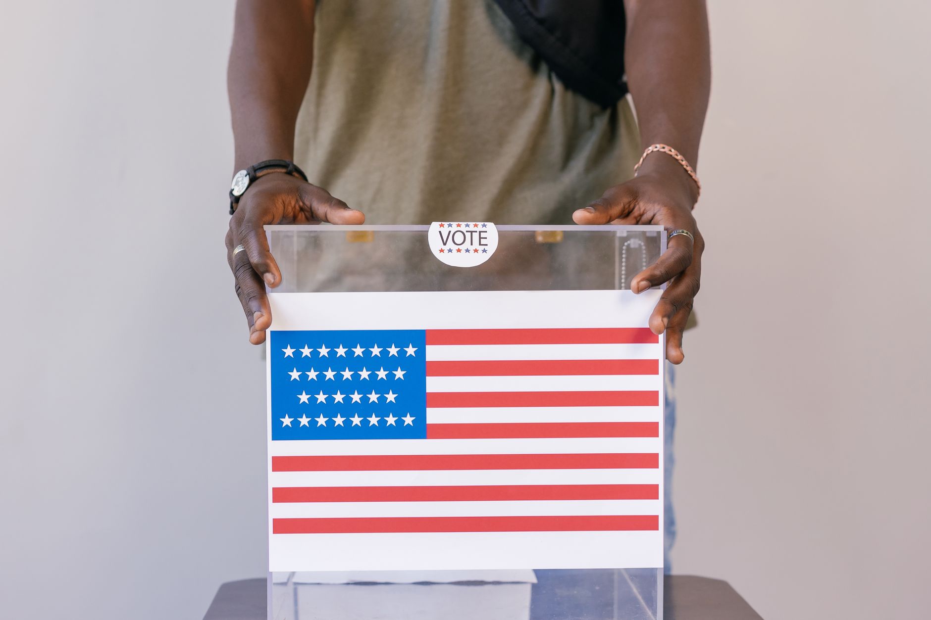 Close up of a person placing a vote in a transparent ballot box with an American flag print.
