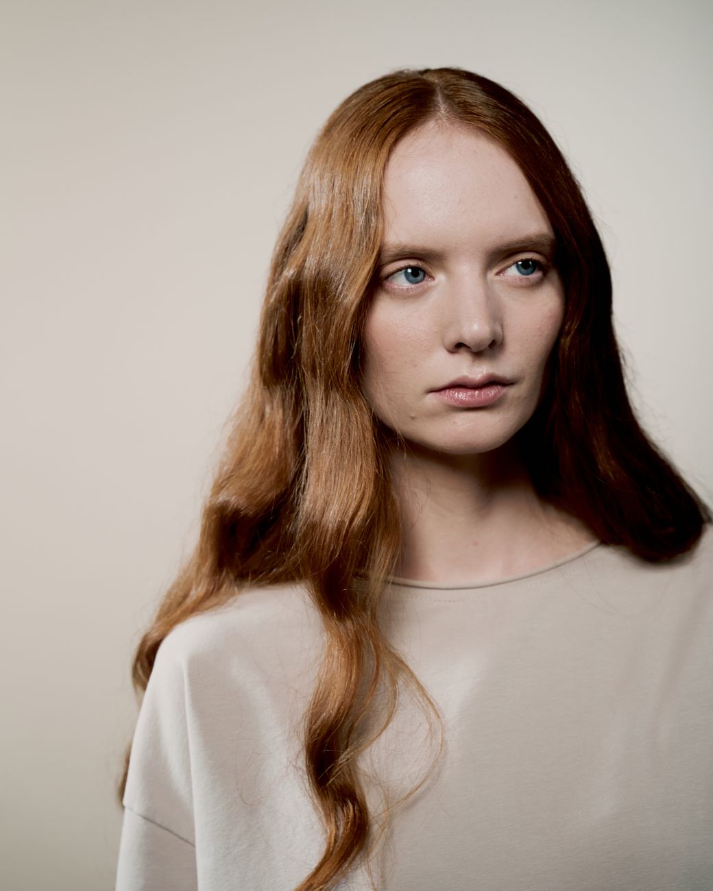 Studio portrait of a young red haired woman with soft lighting and neutral tones.