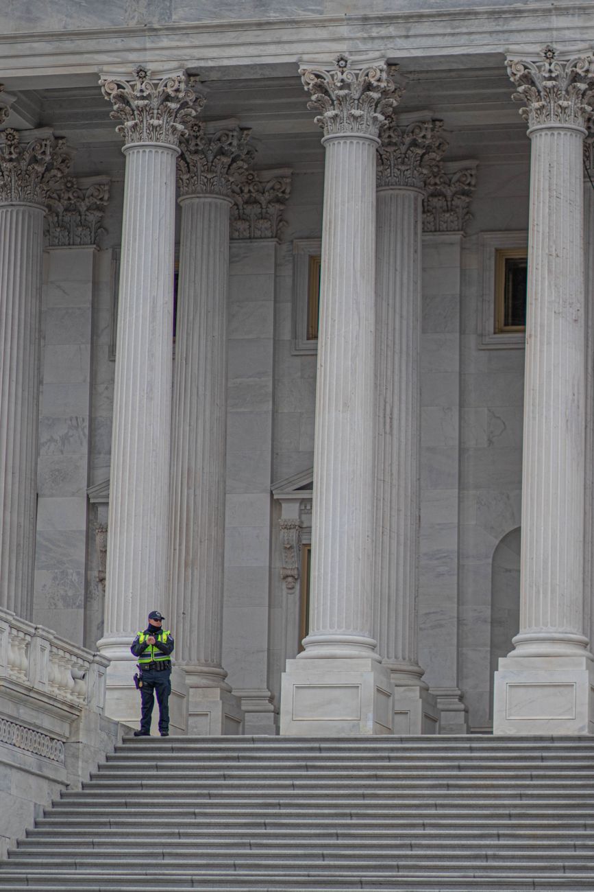 Neoclassical architecture of Capitol Building in Washington, DC, with security presence.