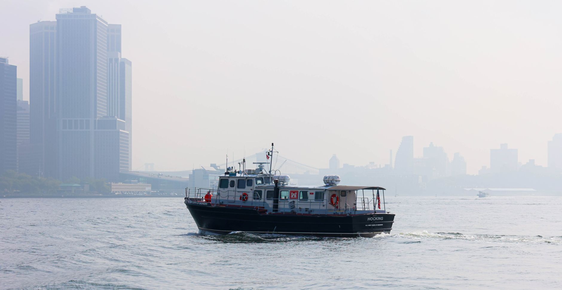 A boat sails on the Hudson River with New York City's iconic skyline enveloped in fog.