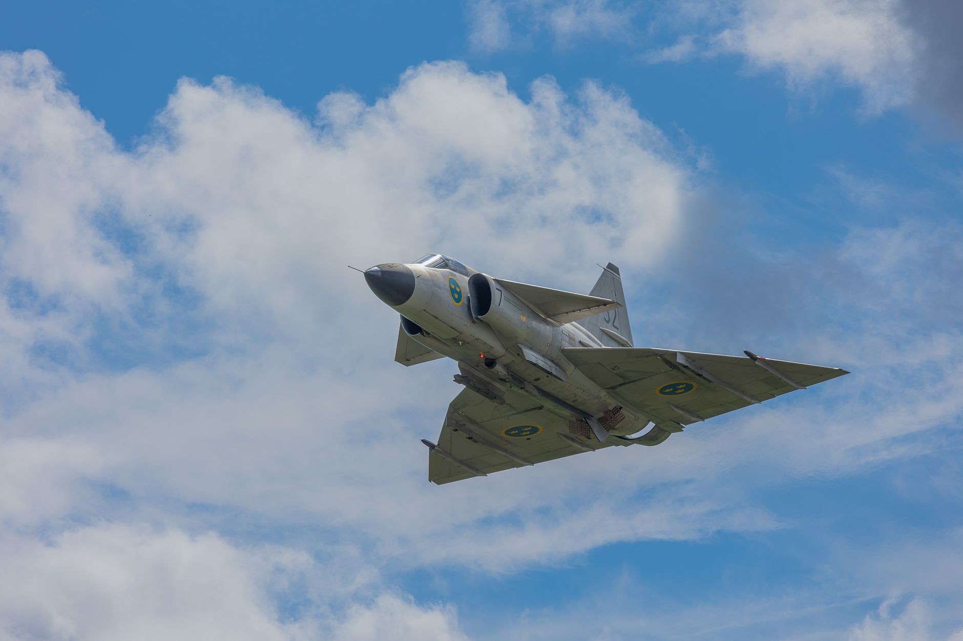A majestic fighter jet flying through a clear blue sky, demonstrating speed and power against fluffy white clouds.