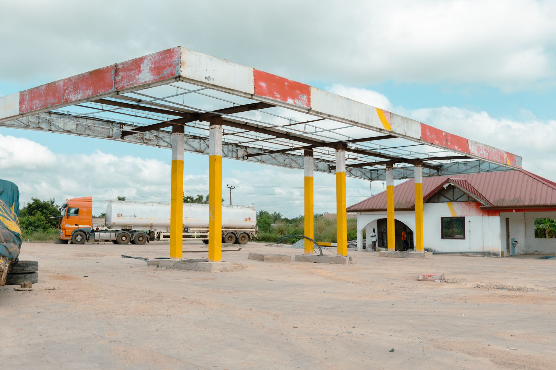 An empty gas station with a parked tanker truck, set in an open outdoor space under a cloudy sky.
