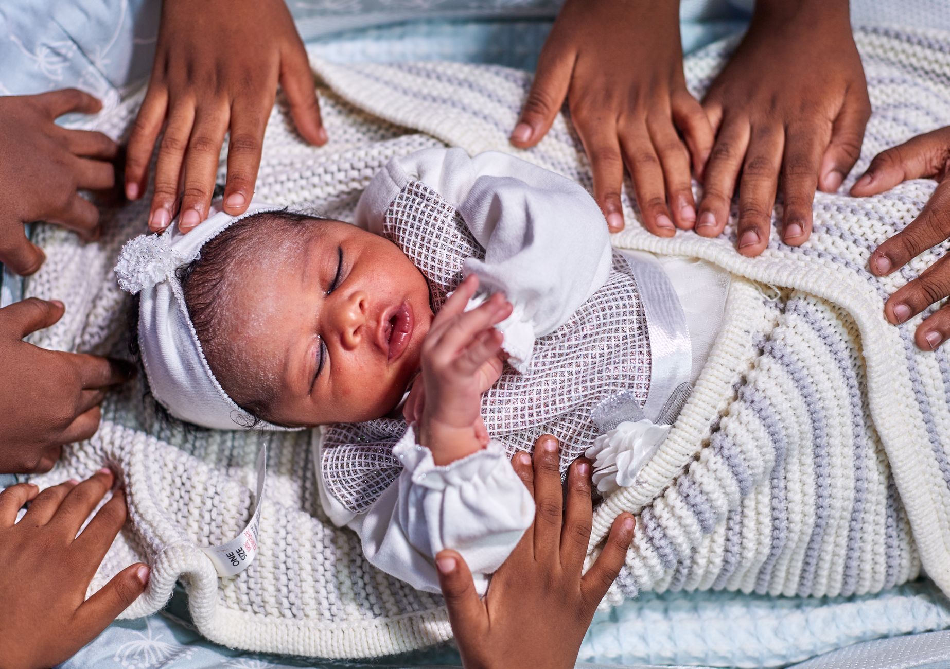 Adorable newborn baby in cozy white outfit surrounded by caring family hands, capturing love and warmth.