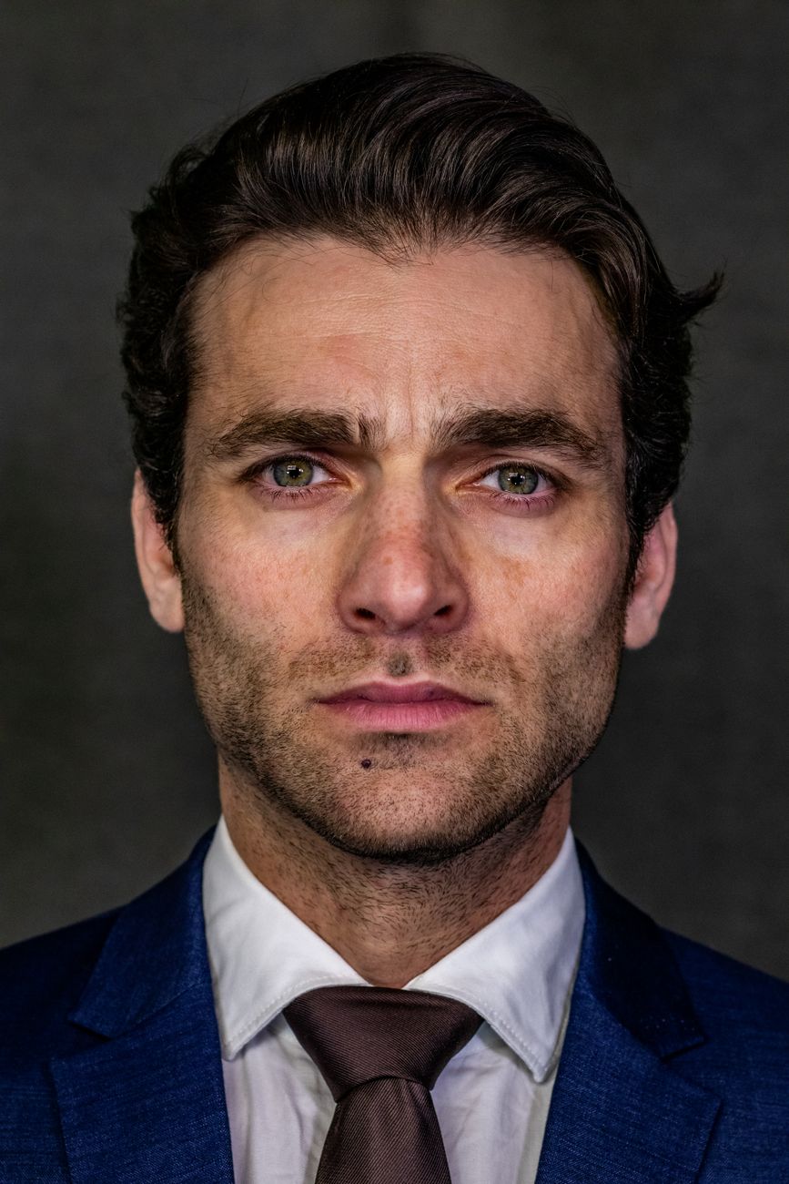 Close up portrait of a businessman in a blue suit and tie against a gray background.