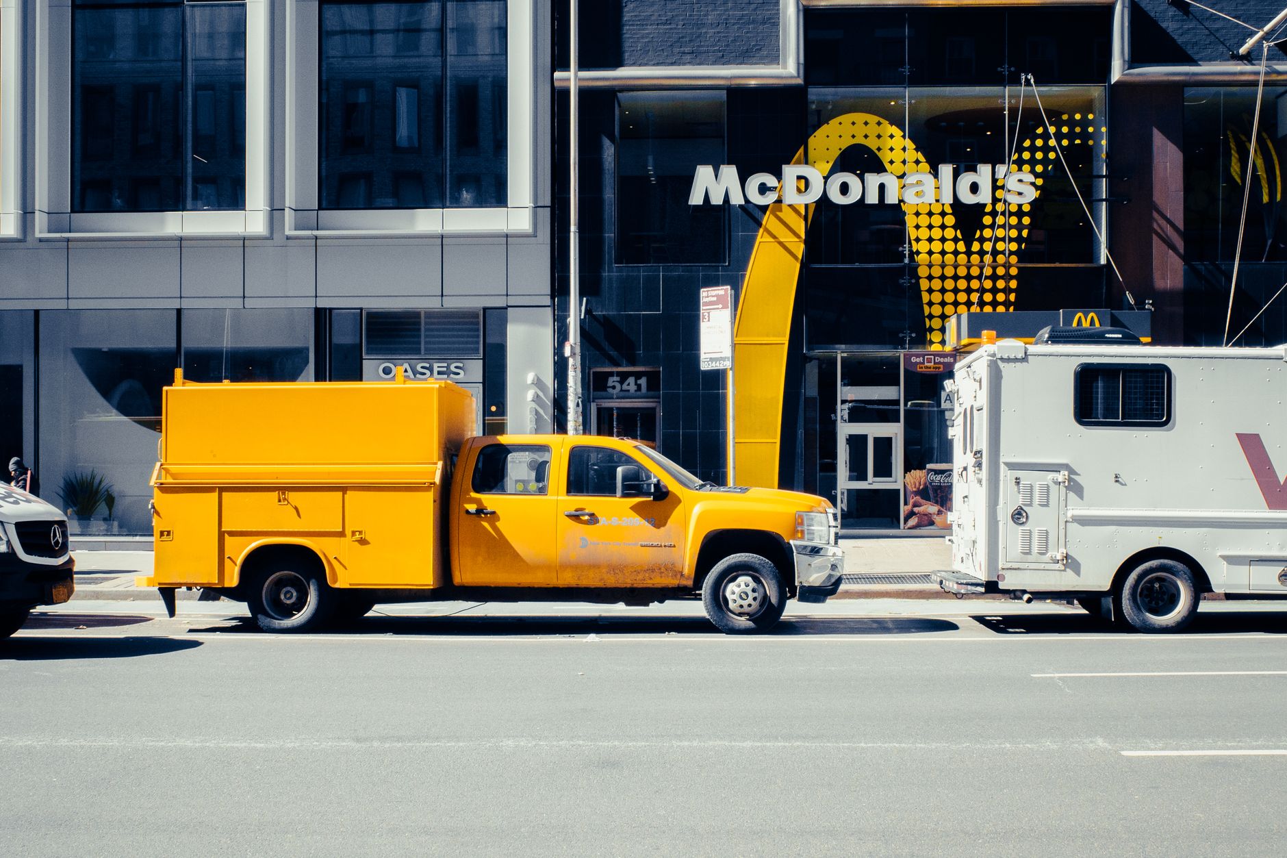 A yellow pickup truck parked in front of a McDonald's in New York City on a sunny day.
