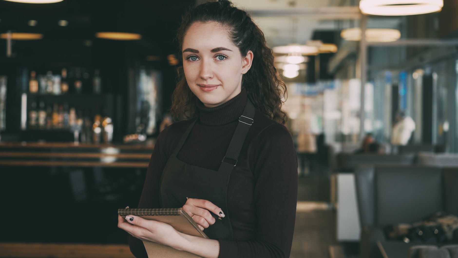 Friendly waitress holding a notepad, ready to take orders in a modern cafe setting.