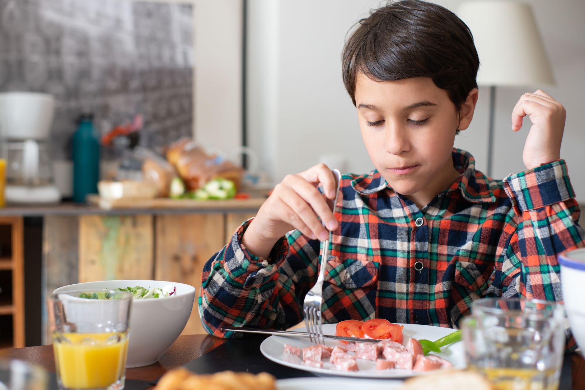 A young boy in a plaid shirt enjoys a nutritious breakfast at home, focusing on good manners and healthy eating habits.