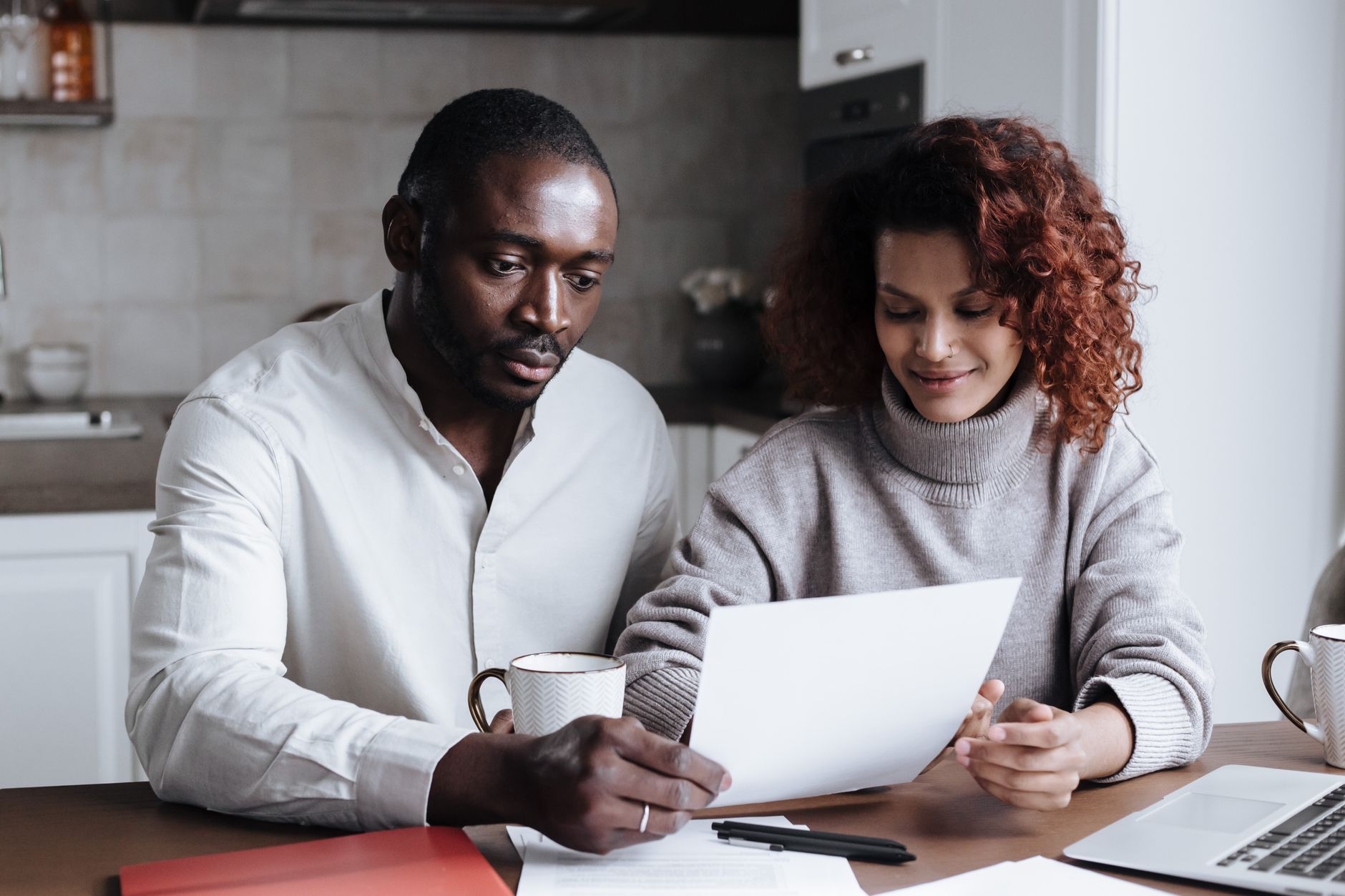 A couple reviews paperwork at a kitchen table, embodying teamwork and collaboration.